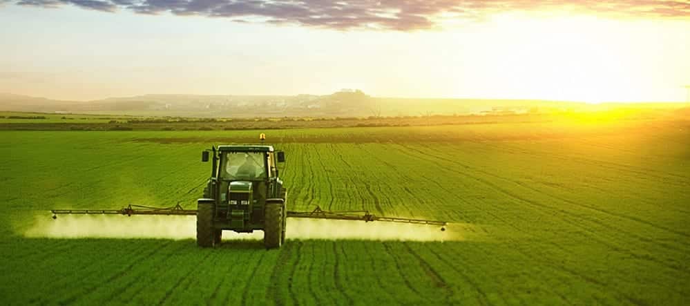 Green Tractor Spraying A Field Of Wheat Stock Photo